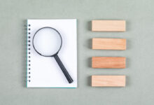 searching-research-concept-with-notebook-magnifier-wooden-blocks-gray-background-top-view-horizontal-image