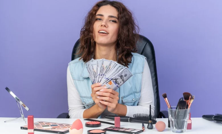 pleased-pretty-caucasian-woman-sitting-table-with-makeup-tools-holding-money